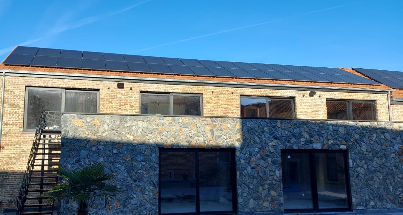 Longue rangée de panneaux solaires noirs sur la toiture en tuiles d’un bâtiment en briques et pierre
